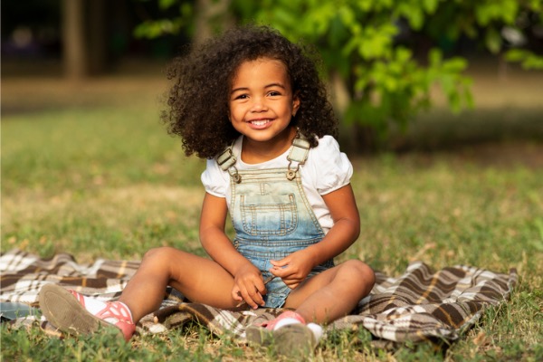 Young girl sitting in the grass smiling at the camera 